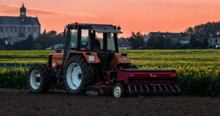 A tractor operates in a field at sunset.