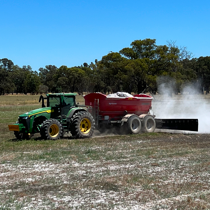 A tractor equipped with a dusting machine sprays granulated fertiliser across a field, ensuring precise application rates.