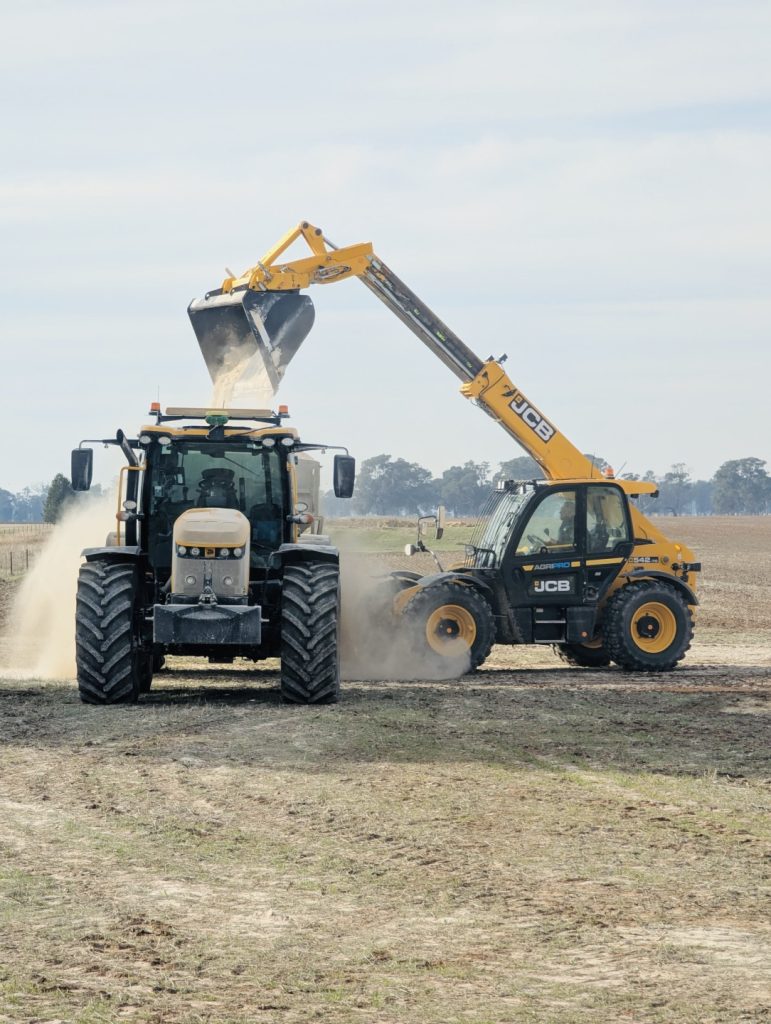 A tractor and loader collaborate on a dirt road, preparing to spread lime and fertiliser.