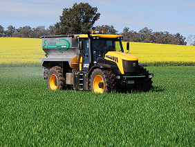 A tractor spraying a field of yellow and green plants, equipped with technology for precise fertilization and spreading.